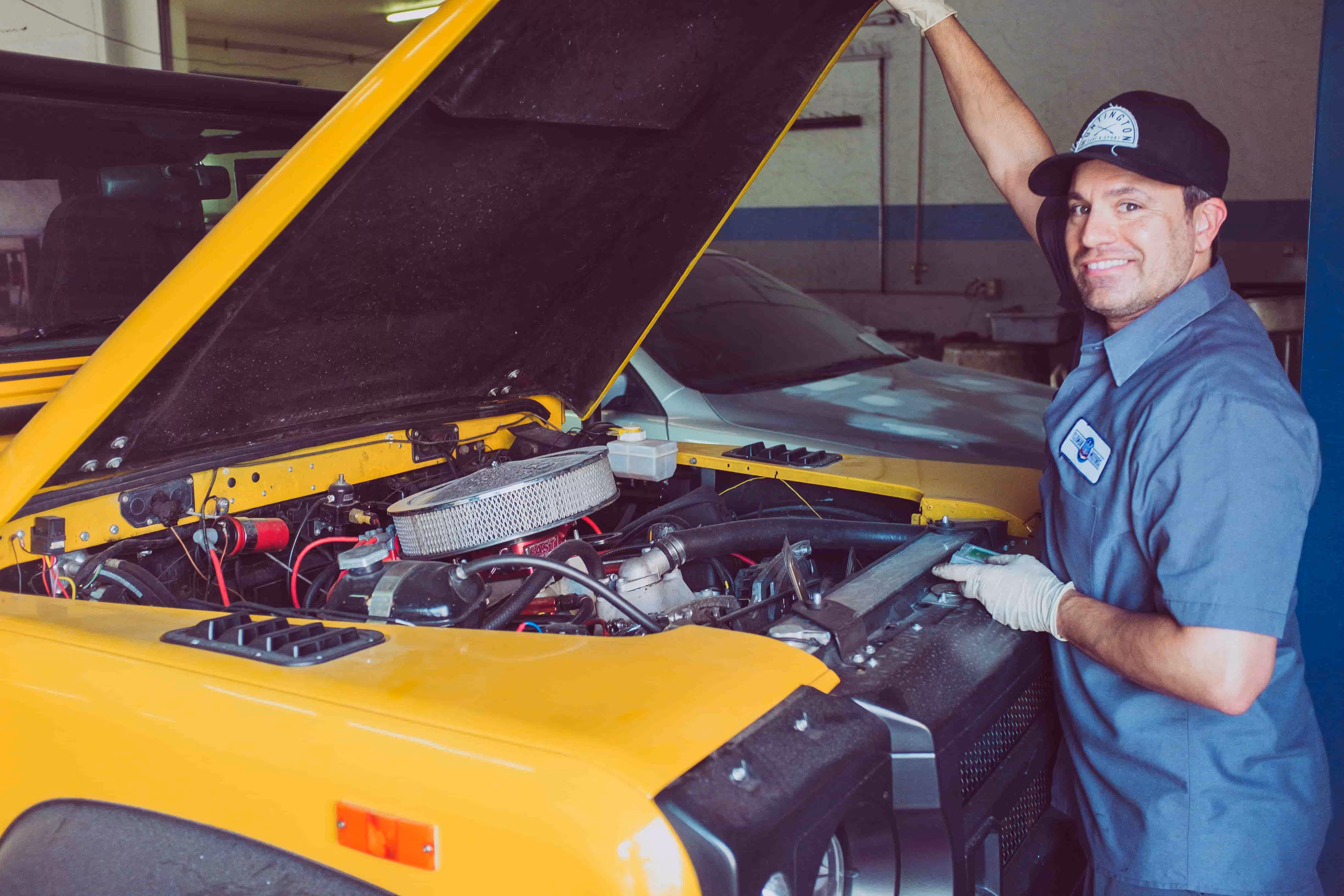 car mechanic smiling as he opens the hood of a truck