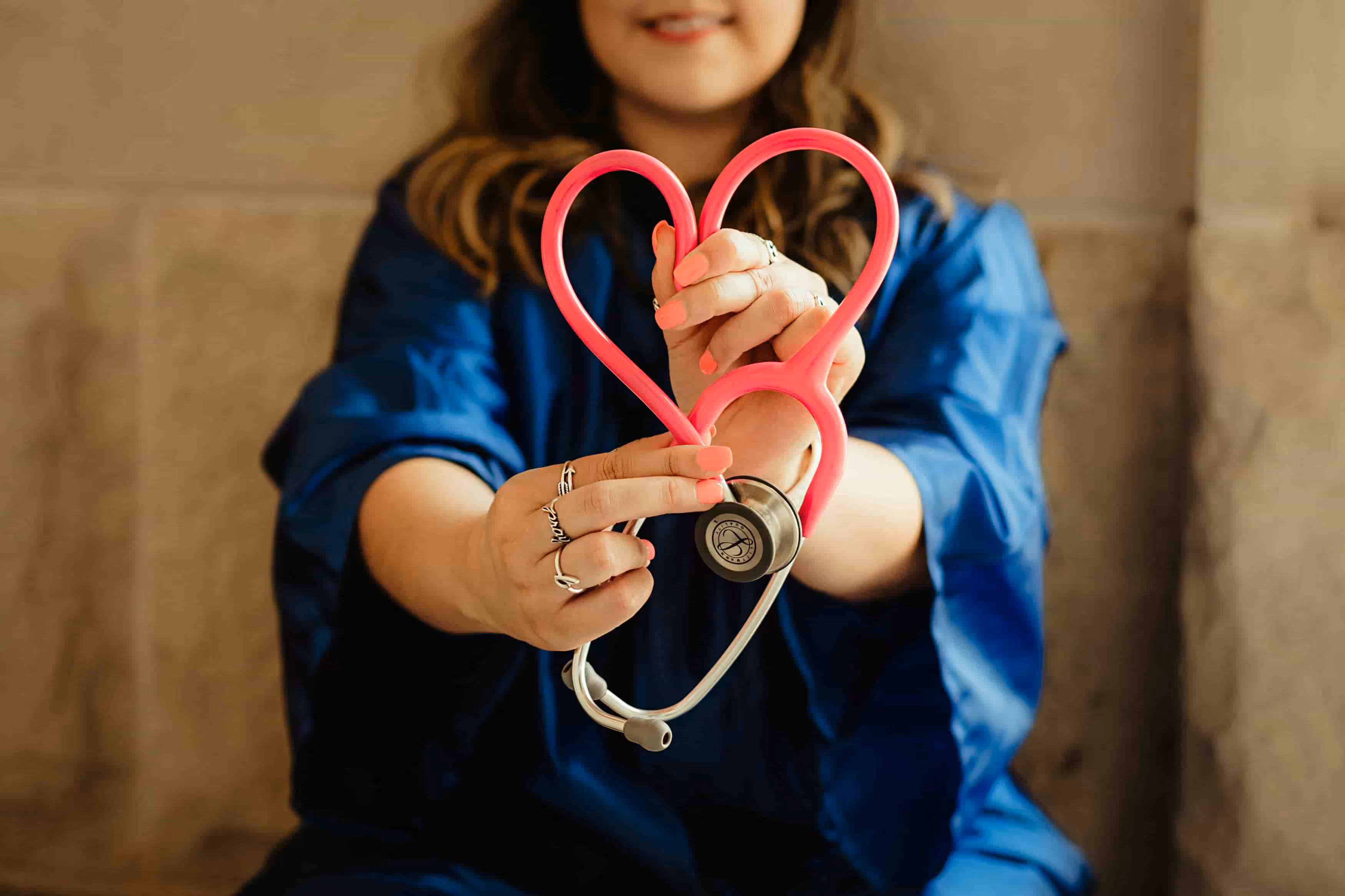healthcare worker holding up a pink stethoscope in the form or a heart